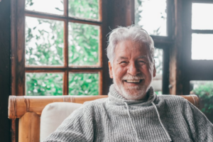 Older man smiling from the comfort of his log cabin