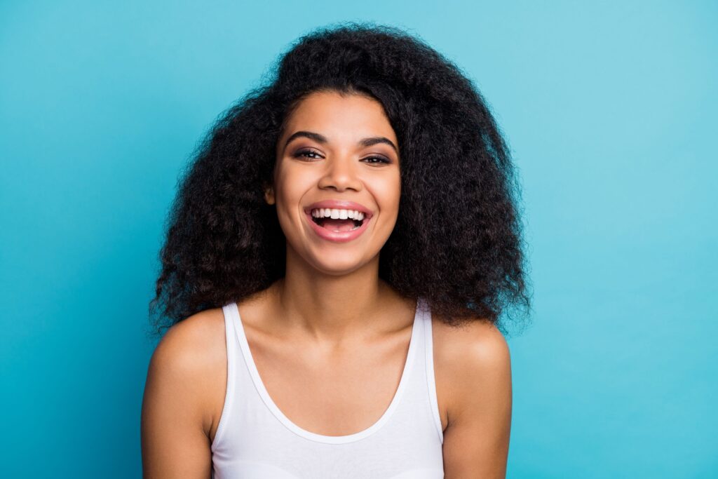 Woman with curly brown hair in white tank top smiling